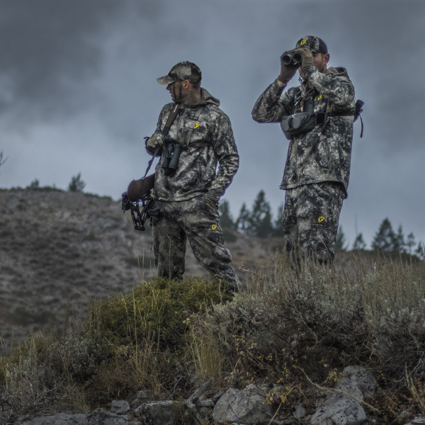 Two men scanning the field for Elk while hunting out west with binoculars, wearing blocker outdoors gear for scent blocking 