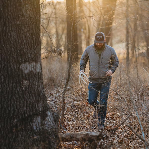 Man carrying a shed antler through the woods near a food source. photo credit Michael Heffernon